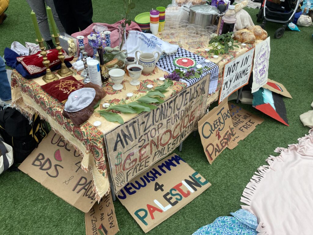 A shabbat table set-up at the UBC encampment is adorned with signs that say "Anti-Zionism is not Anti-Semtism" "Jewish Mama 4 Palestine" and others.
